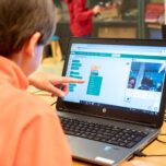 CoderDojo geeft codeerworkshop, jongen zit achter laptop en wijst naar scherm.