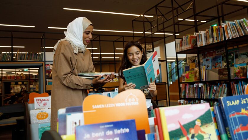 Moeder en dochter tussen schappen met kinderboeken in bibliotheek